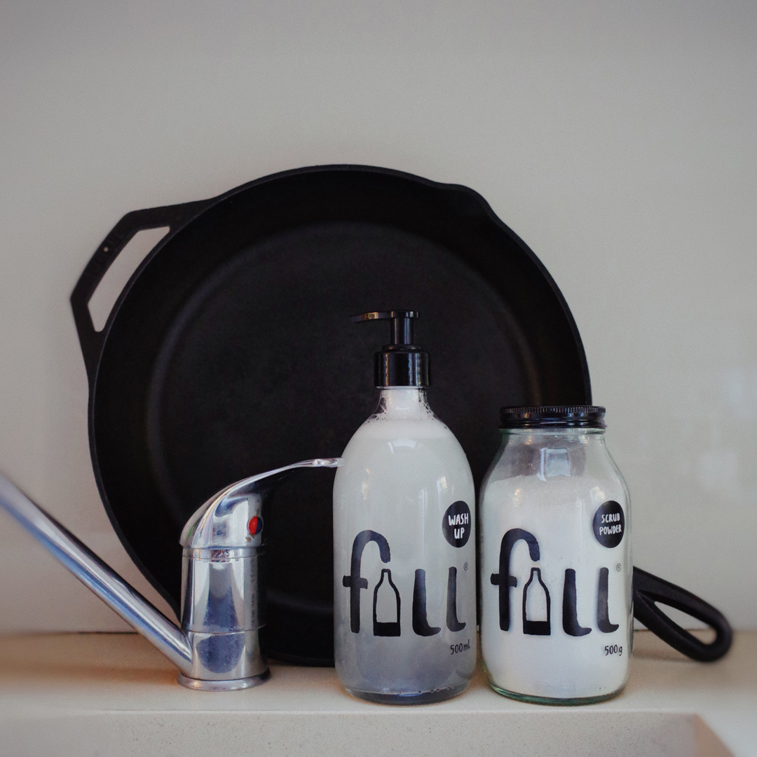 Wash Up and Scrub powder next to a pan by a kitchen tap