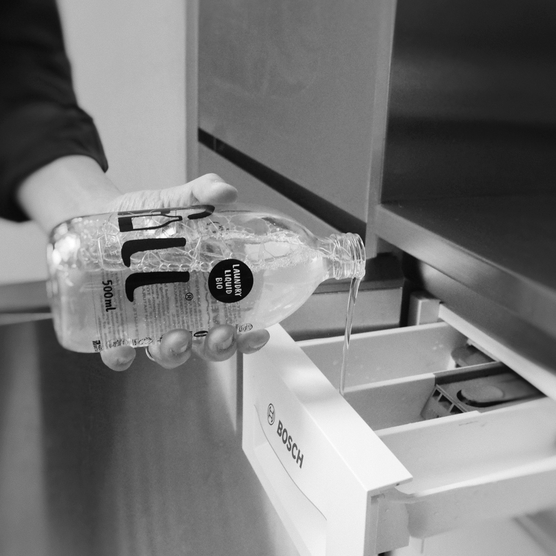 Hand pouring Laundry Liquid Bio into washing machine compartment